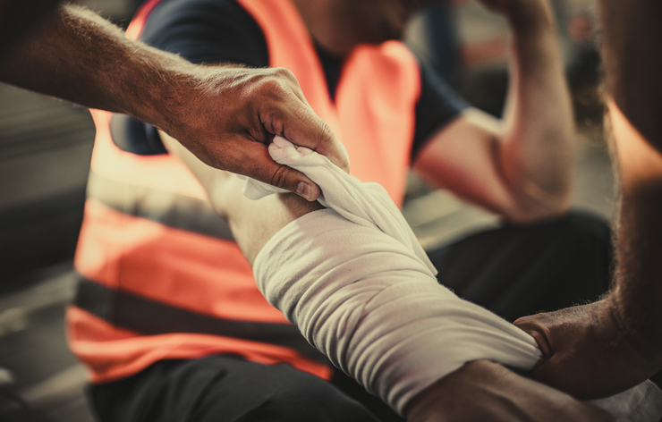 Close up of unrecognizable manual worker assisting his colleague with physical injury in a warehouse.